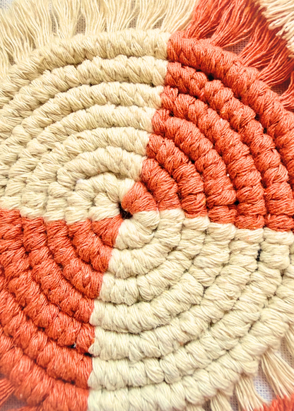 Close-up detail of a handmade terracotta and off white macramé coaster showing soft cotton knots and fringe texture.