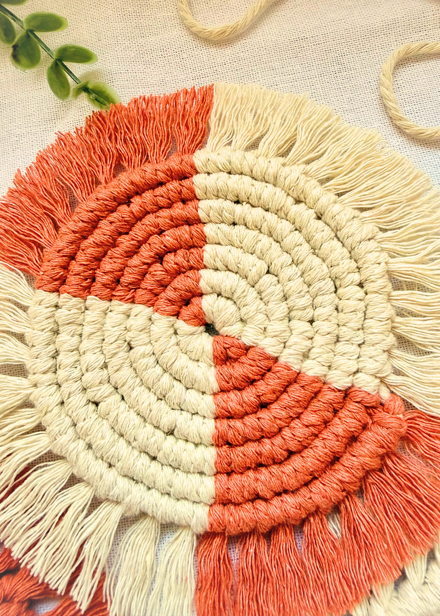 Detailed view of a terracotta and natural cotton macramé coaster with spiral knot pattern and fringe edges.