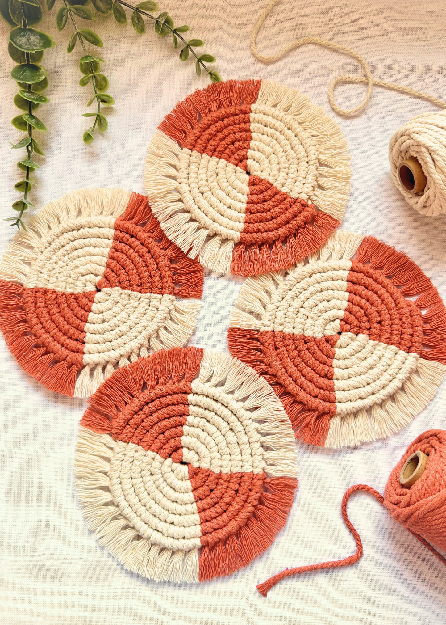 Set of four handmade terracotta and off white macramé coasters arranged on an off white background with cotton cord styling.