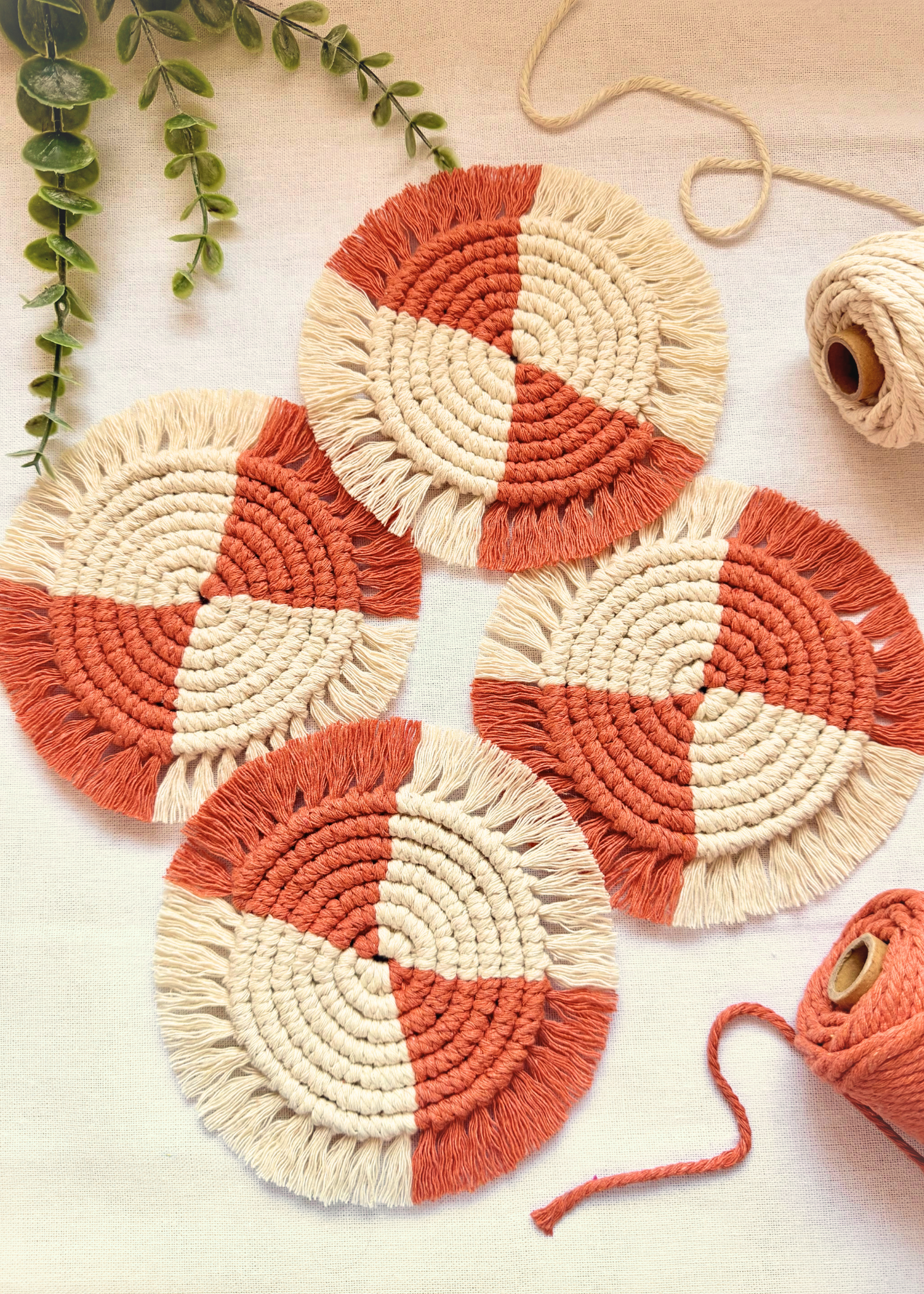 Set of four handmade terracotta and off white macramé coasters arranged on an off white background with cotton cord styling.