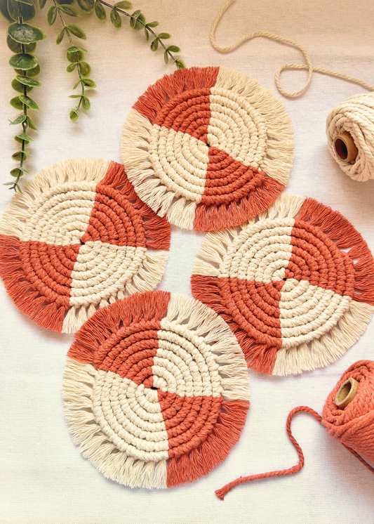 Set of four handmade terracotta and off white macramé coasters arranged on an off white background with cotton cord styling.