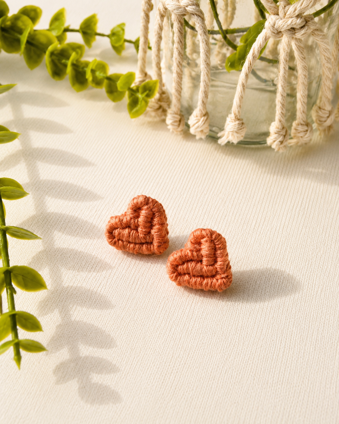 Terracotta handmade macramé heart stud earrings on a neutral fabric background.