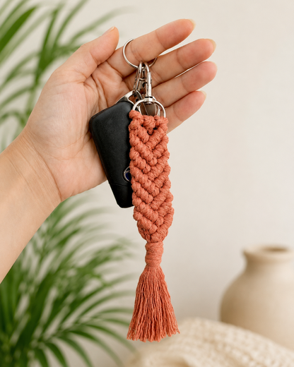 Hand holding a terracotta macrame keychain attached to car keys with tassel detail and boho style.
